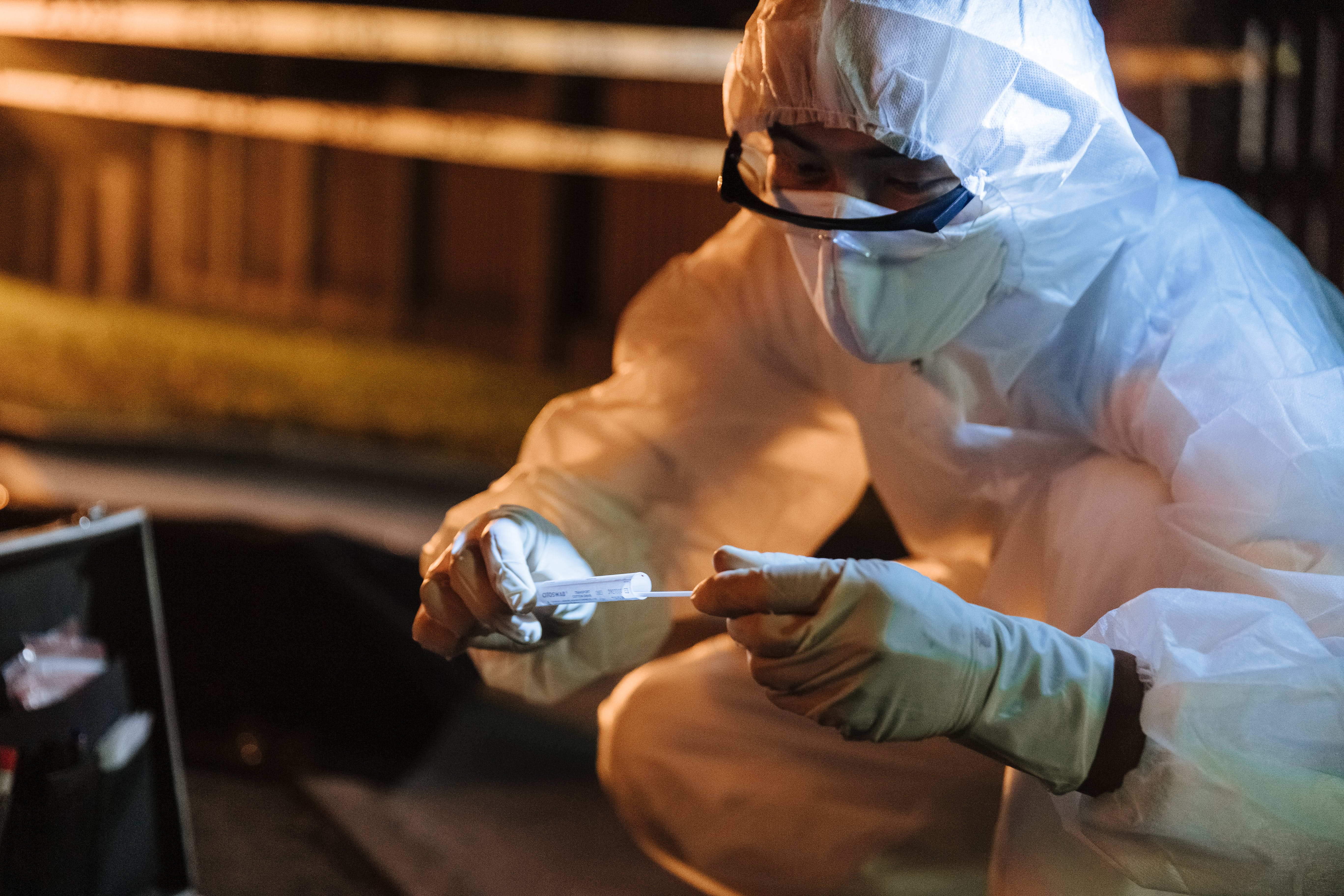 photo of a man dressed in a protective suit taking a sample into a vial for testing